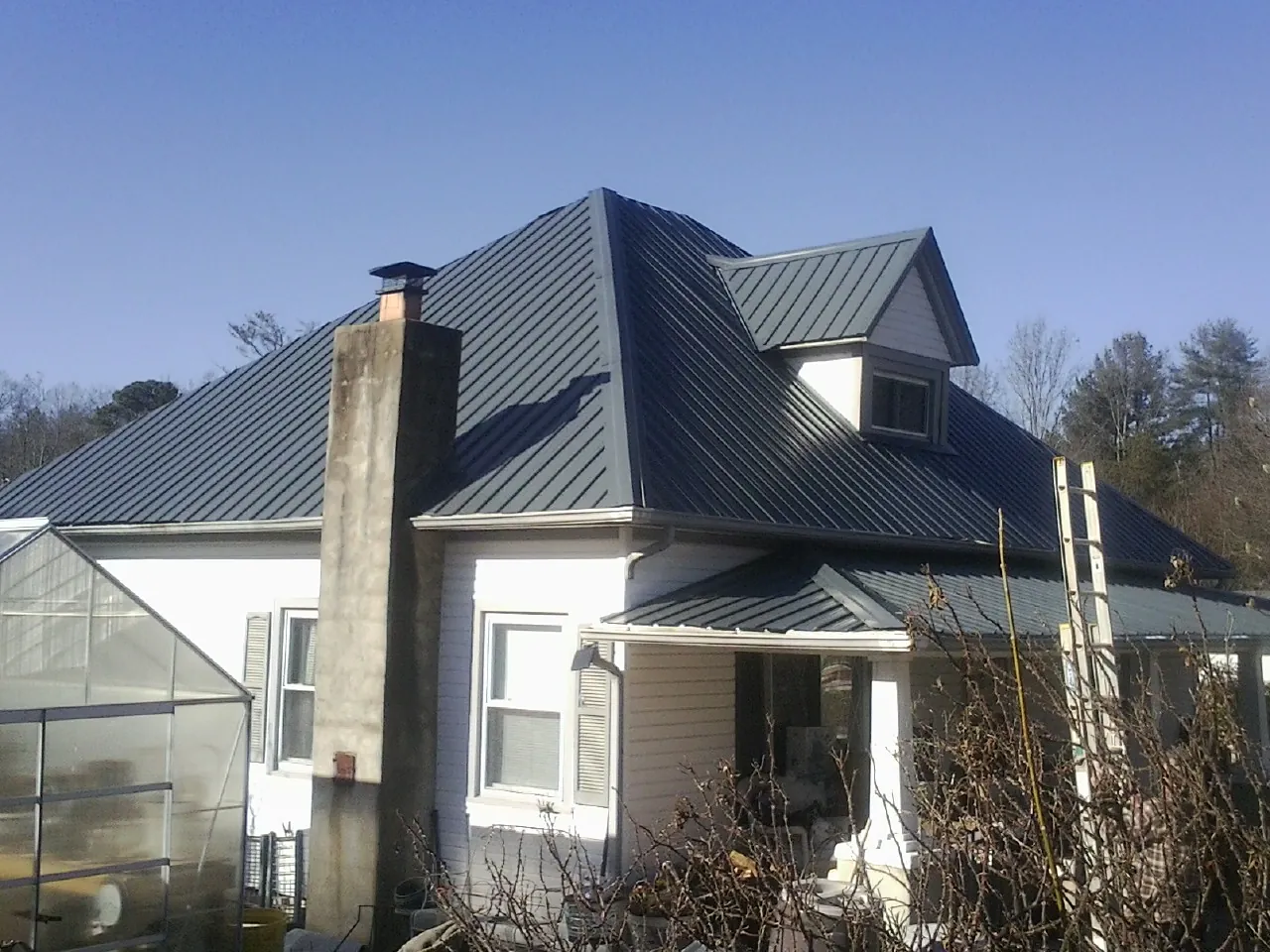Dark blue standing seam metal roof on a white farmhouse with dormer — Slate & Tile Roof Repair by Roofing Brothers in Bascom