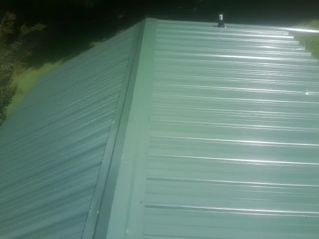New green metal panels meeting at the ridge of a roof — Flat Roof Repair work by our crew in Bascom